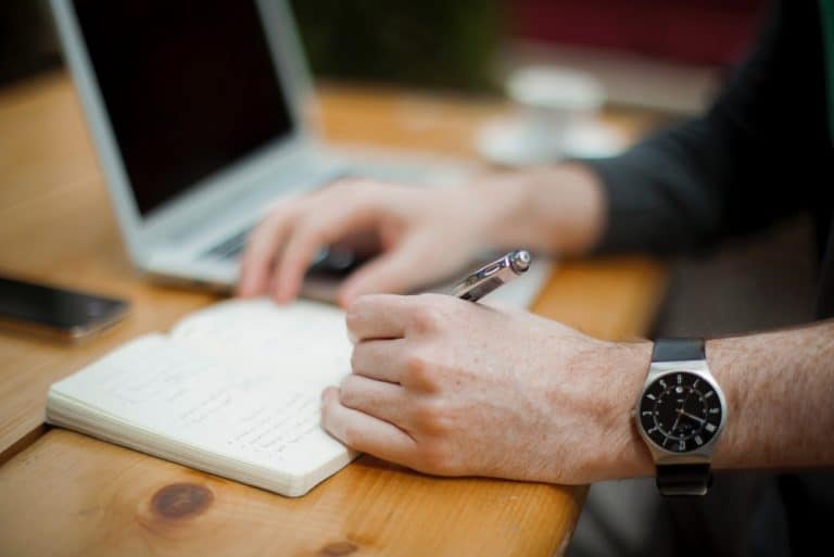 man writing in notebook sitting at desk