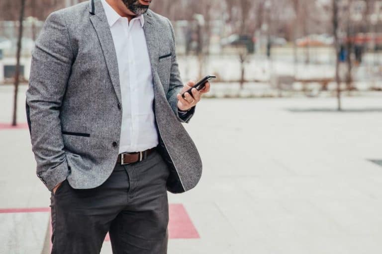 middle shot of business man on his phone next to a park