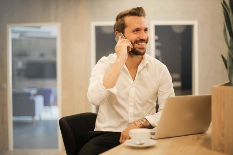 smiling business man sitting at his office desk on his laptop with a coffee cup