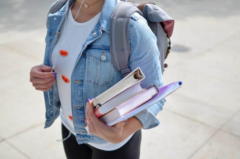 university student with backpack, headphones and holding text books walking to Univeristy
