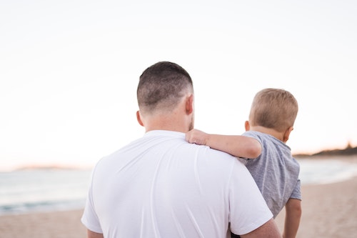 father carrying his son while walking on the beach