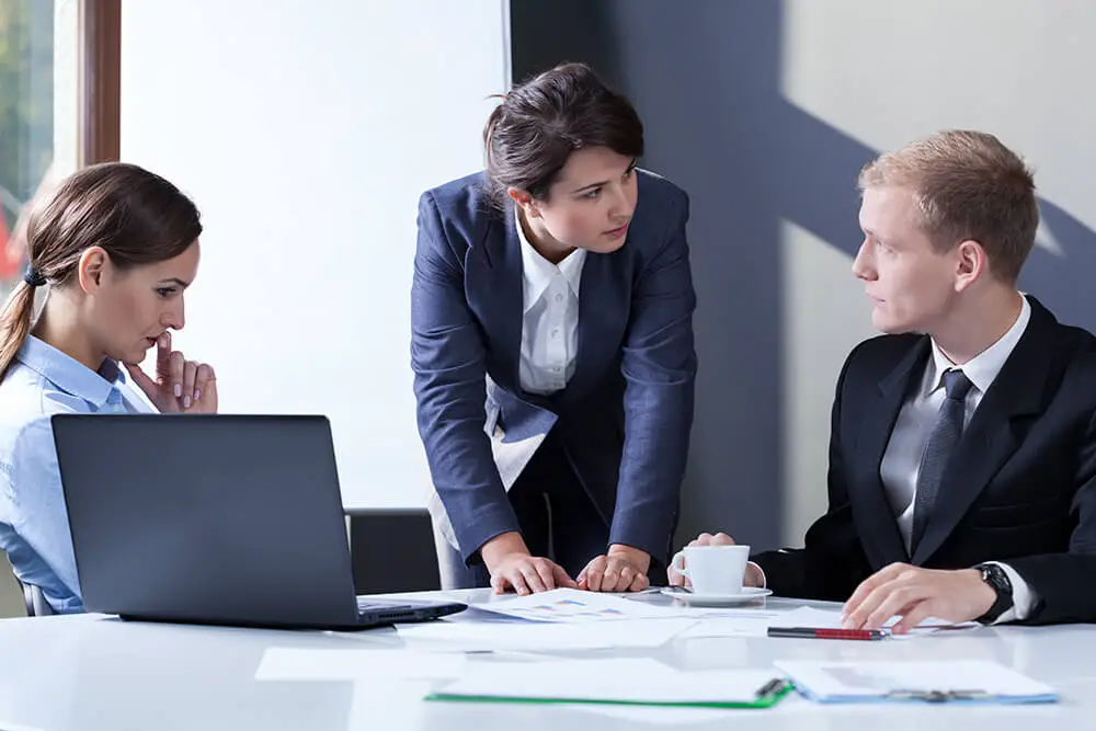 Female office worker leaning over table talking to man