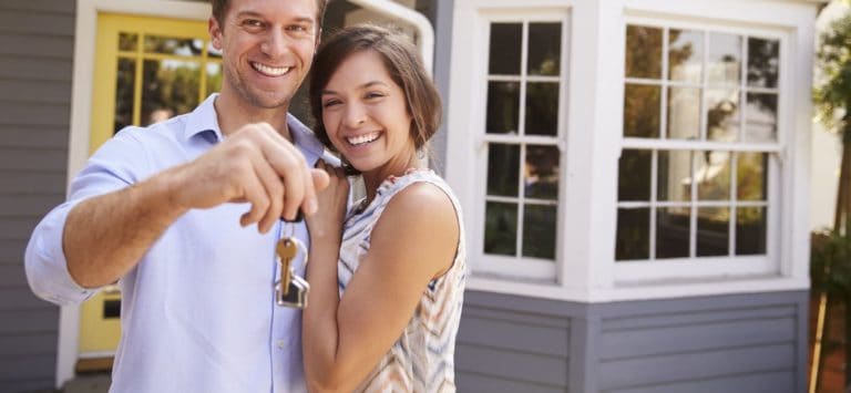 a couple with keys standing outside the new home