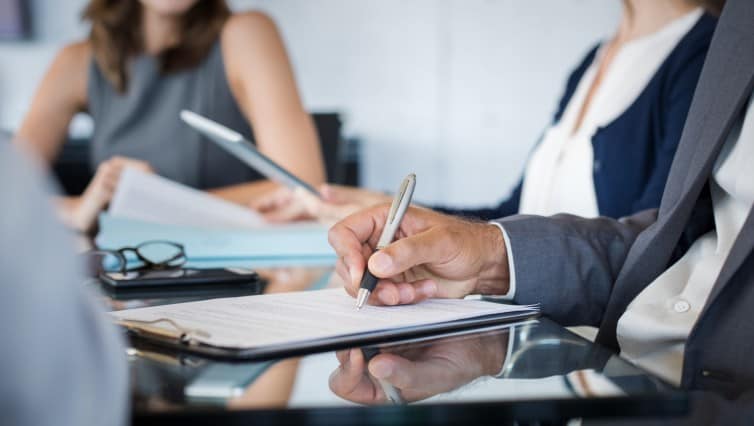 A group of business people sitting at a table and signing a document to address an Unconscionable Conduct case involving Special disadvantage.