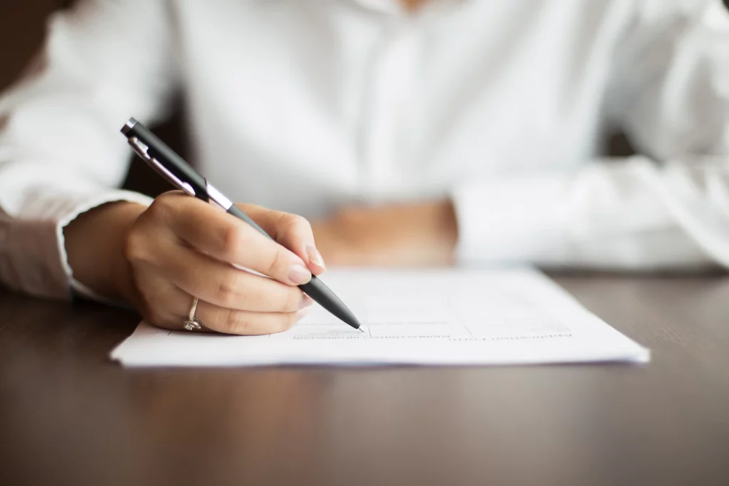 A woman drafting a Share Sale Agreement or Business Sale Agreement with a pen.