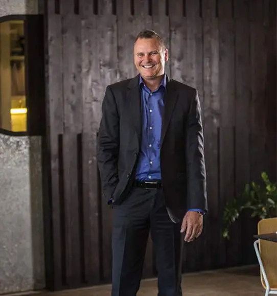 A man in a suit standing in front of a wooden table.