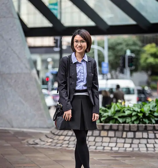 A woman in a skirt and blazer standing on a sidewalk.